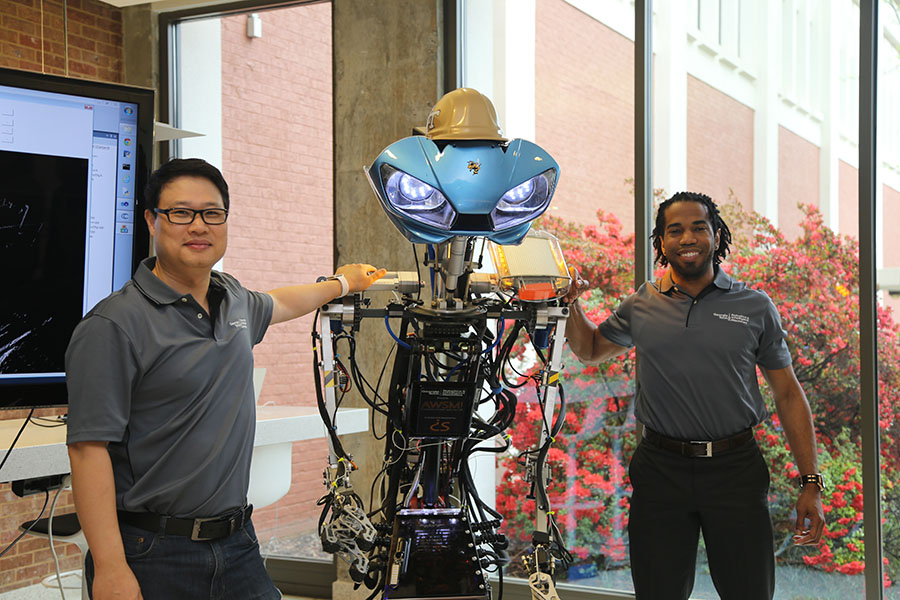 Associate Professor Yong Cho, left, and Dimitri Seneca Snowden pose with the robot Snowden built to help teach underprivileged children about robotics and inspire them to chase their dreams. Snowden has donated the machine to Cho's Robotics and Construction Automation Laboratory in the School of Civil and Environmental Engineering, where they'll work together to update and adapt the robot to open new areas of construction research. Snowden calls himself an ontological architect, saying he studies how the things we design for our world design us back. (Photo: Jess Hunt-Ralston)
